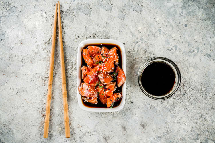 A bowl of tamari and chopsticks next to marinated salmon