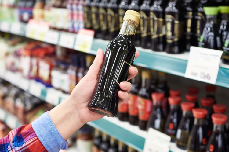 A person taking a bottle of tamari from a grocery store shelf