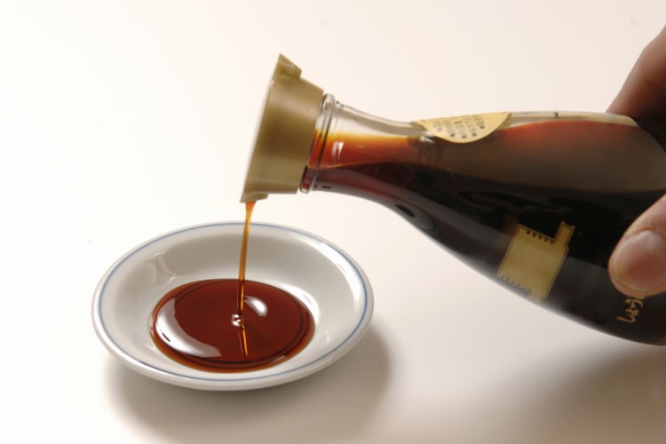 A person pouring soy sauce into a dish