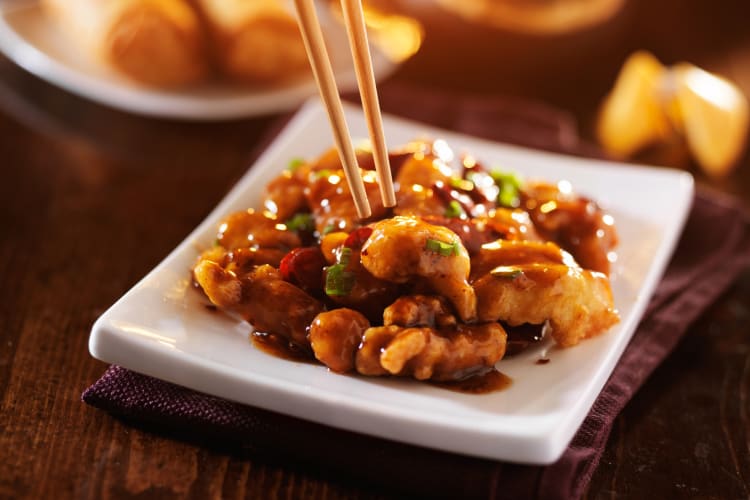 A person using chopsticks to pick up tofu in a sauce