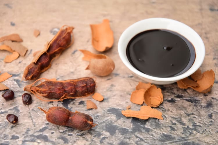 A bowl with tamarind paste next to tamarind pods