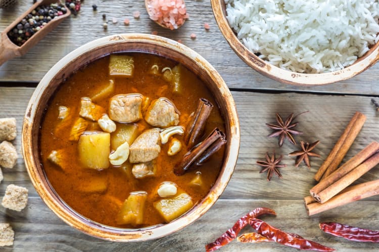 A bowl of curry and a bowl of rice surrounded by spices