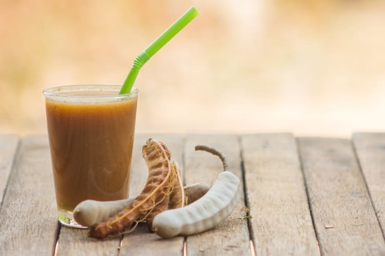 A glass of tamarind juice next to tamarind pods