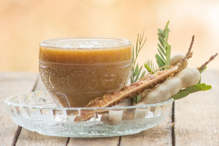 A glass cup with tamarind juice next to tamarind pods