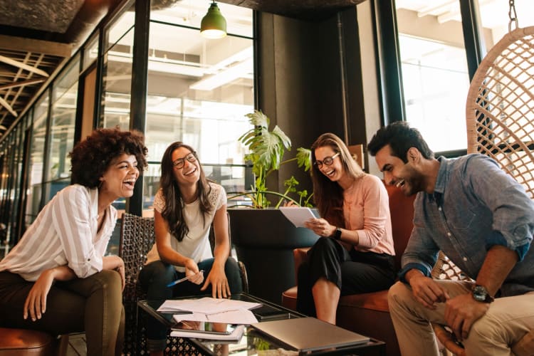Four people laughing in a workplace environment