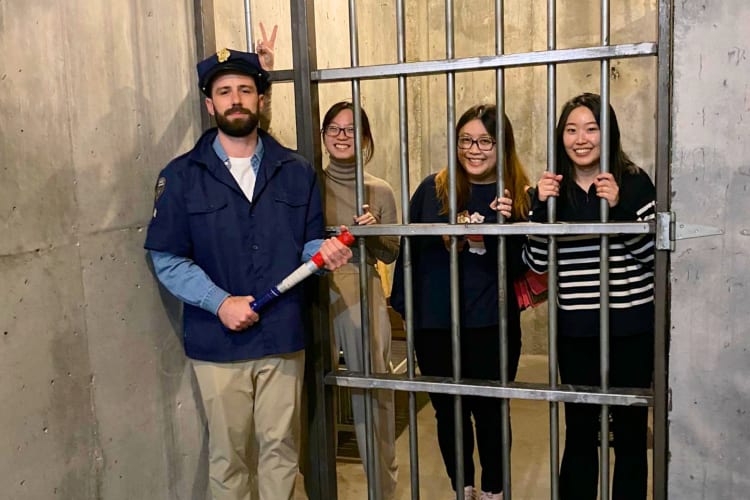 Three people in an escape room jail cell with a guard