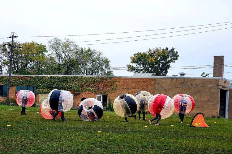 A group of people in large plastic bubbles on the grass