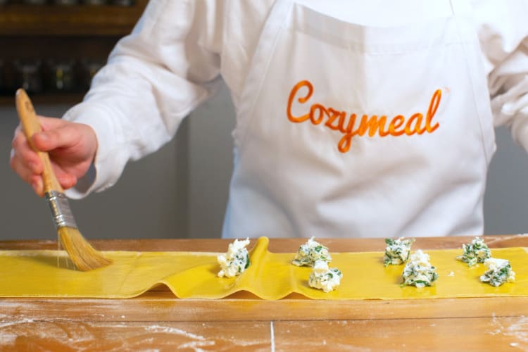 A person in a Cozymeal apron making fresh pasta