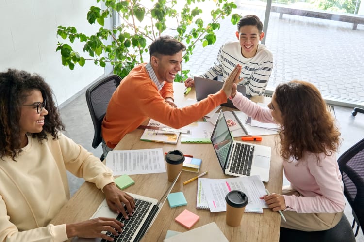 Two co-workers high-fiving at a table with two other colleagues 