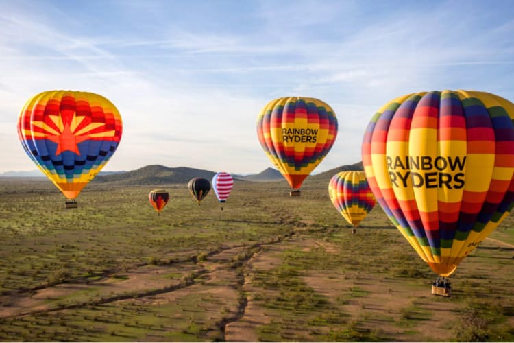 Colorful hot air balloons in the sky next to small hills