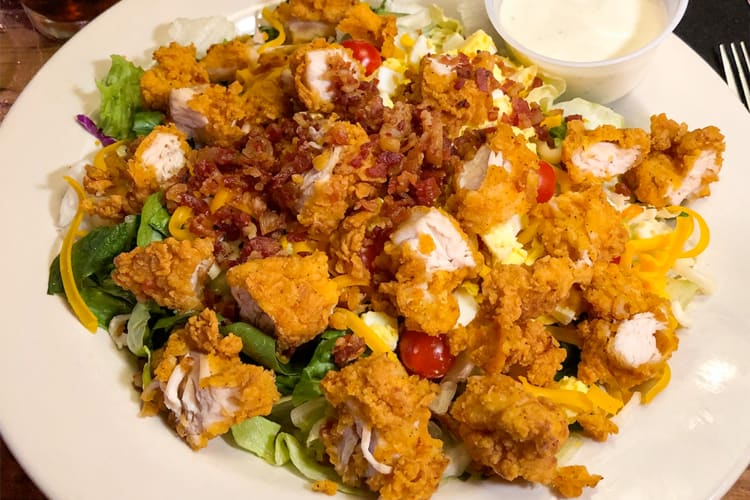 A salad with breaded chicken and bacon bits