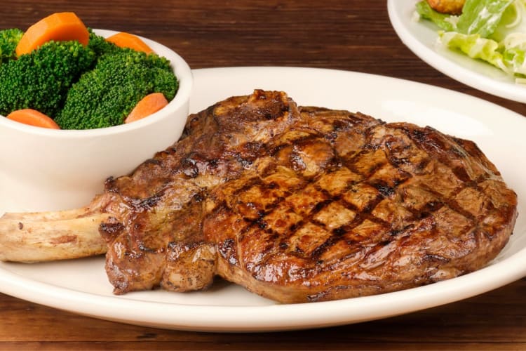 A steak next to a side of steamed vegetables