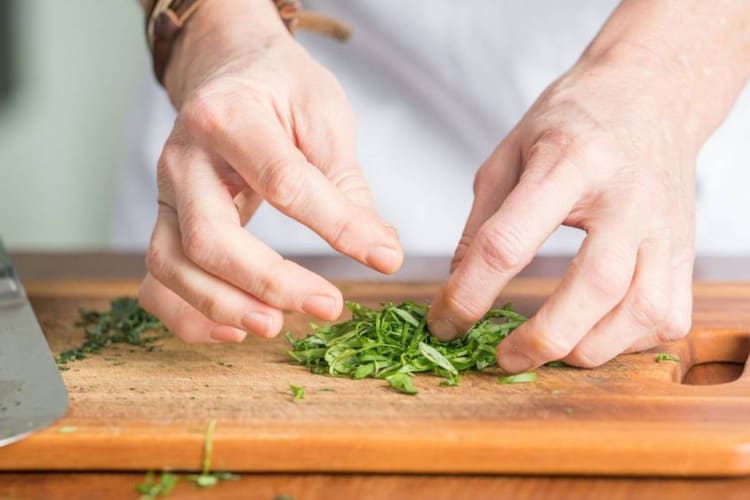 A person chopping basil on a wooden chopping board