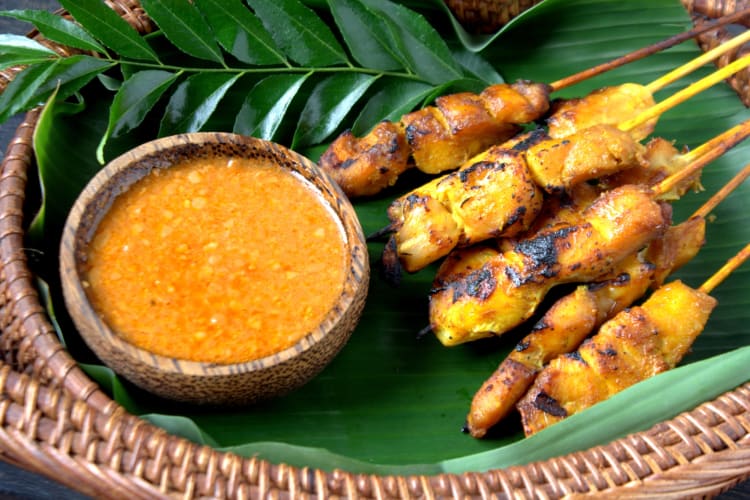 Chicken skewers next to a bowl of satay sauce