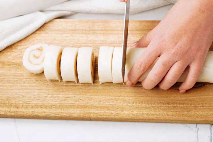 A chef slicing a roll of potato candy into bite-sized pieces.