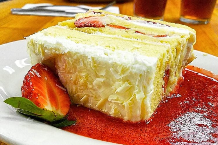 Close-up shot of a slice of wedding cake, half a strawberry and syrup, from The French Pantry