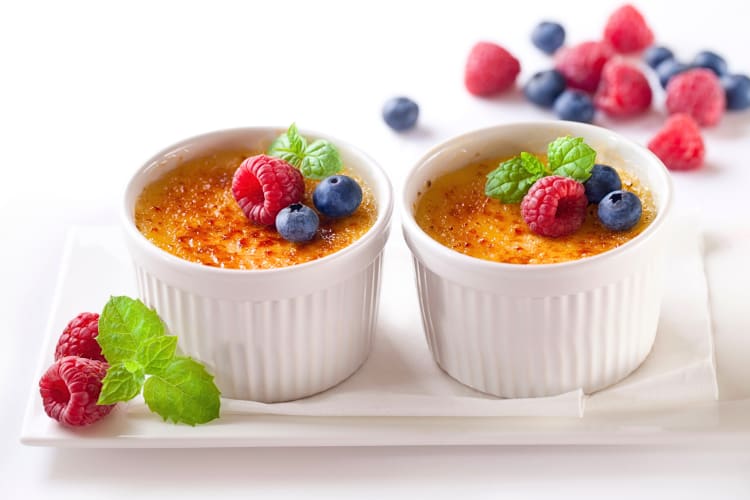 Two bowls of crème brûlée topped with fruit
