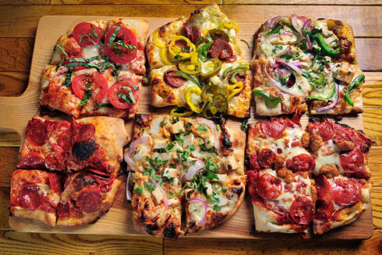 Aerial view of six small pizzas cut in quarters on a wooden serving board, from The Mitten Brewing Co.
