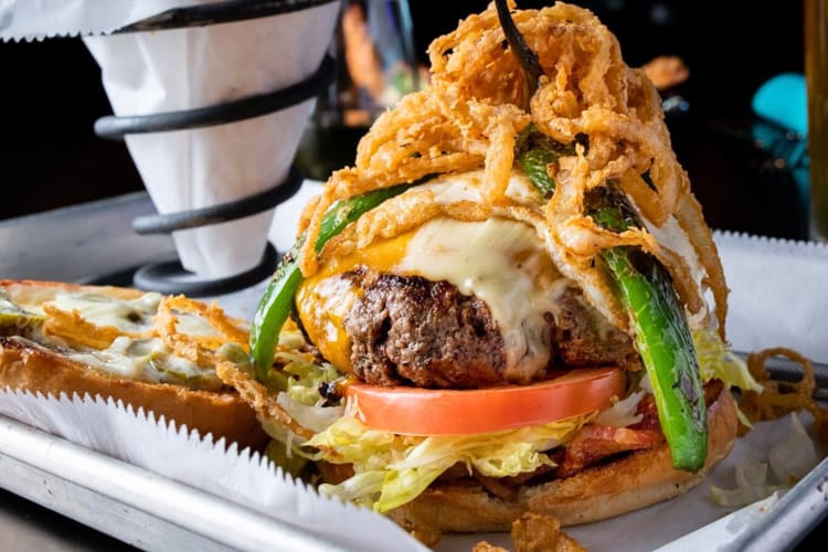 Burger with cheese, lettuce, tomato, jalapeños and onion rings from The Rim