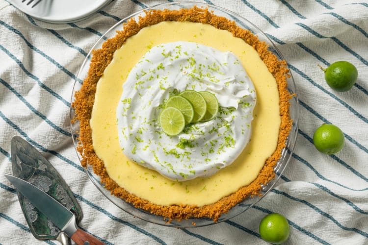 A Key lime pie next to Key limes and cutlery