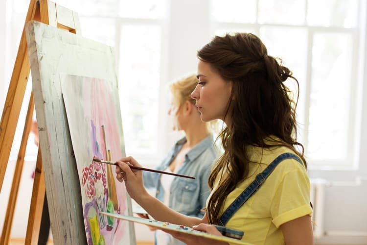 Two girls painting, one in the foreground and the other in the background, representing teen birthday party ideas