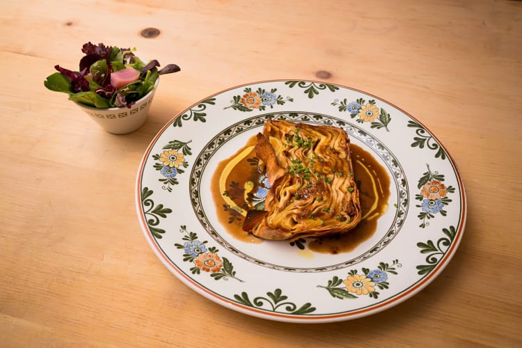 Serving of timballo on a plate next to a small bowl of salad