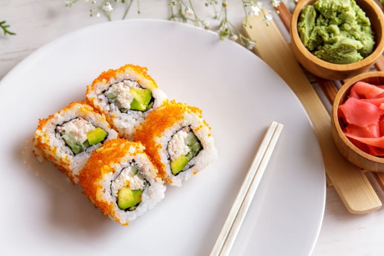 Sushi rolls with orange tobiko next to wasabi and pink ginger