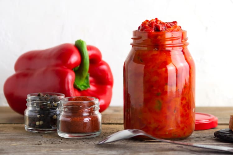 A glass jar with a red sauce next to a red pepper
