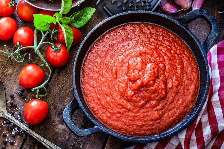 A cast iron pan with tomato sauce surrounded by ingredients