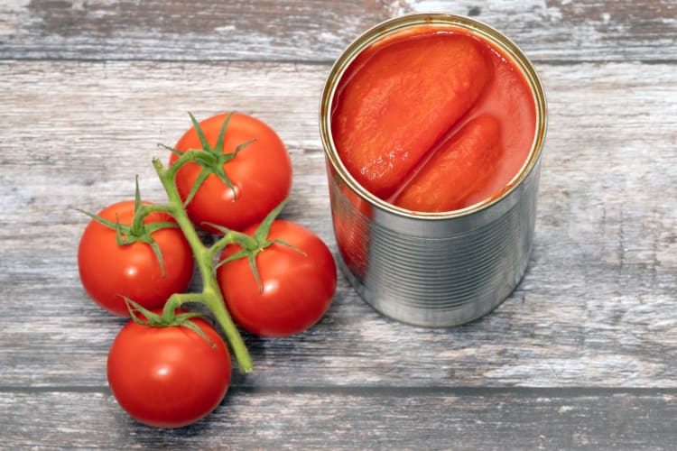 A can of tinned tomatoes next to fresh tomatoes
