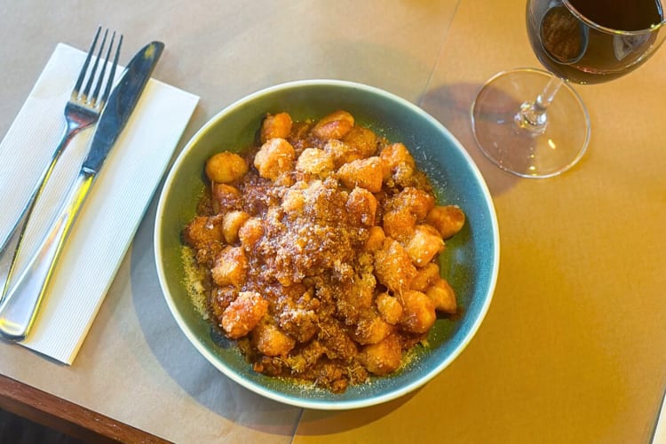 Aerial view of gnocchi Bolognese in between a knife and fork, and a glass of wine