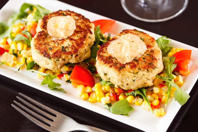 Two crab cakes topped with sauce, on a bed of vegetables