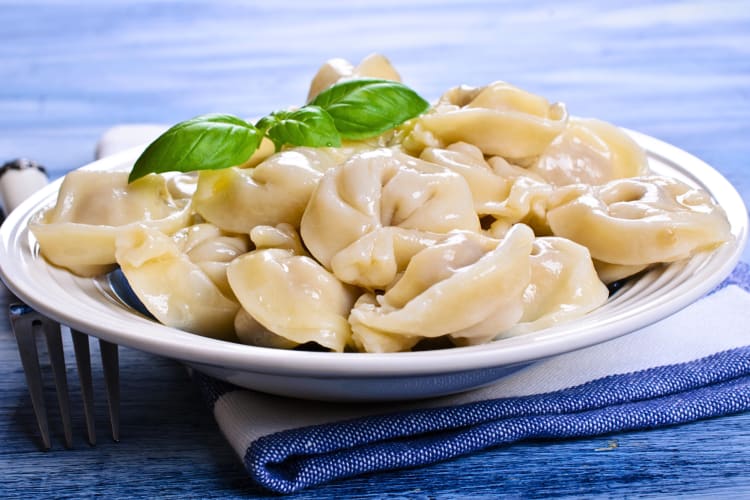 Eye-level view of tortelli in a bowl, topped with basil