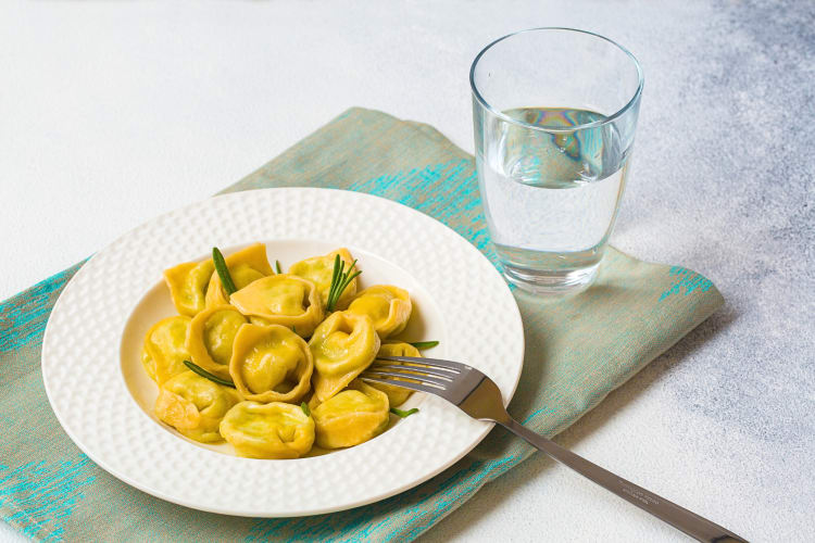 Tortelloni on a plate next to a glass of water