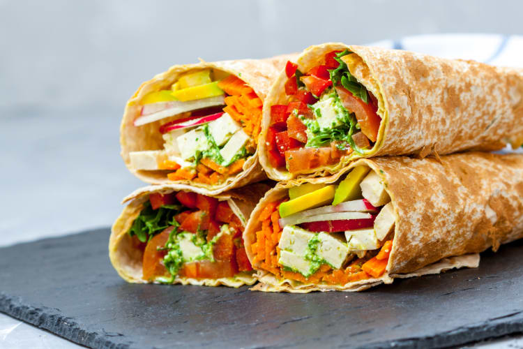 Four tortillas with a variety of fillings in them on a stone serving plate