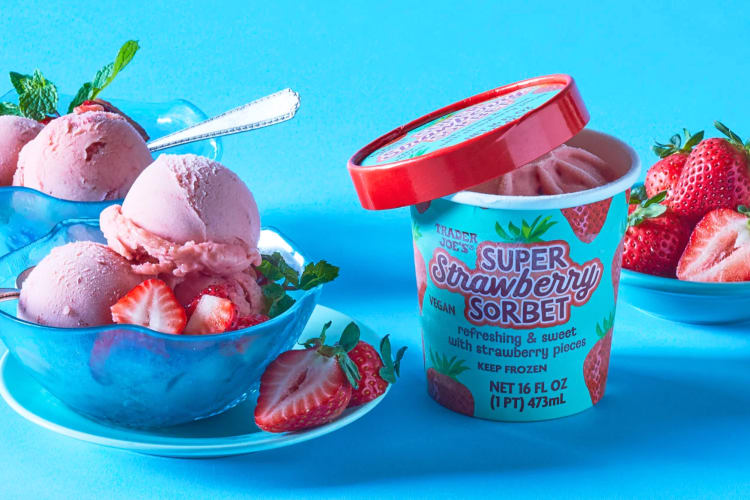 Bowls with strawberry ice cream next to a tub of ice cream and fresh strawberries