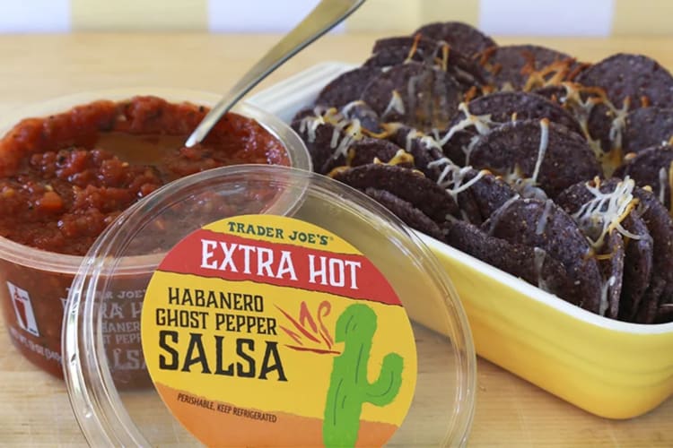 A tub of extra hot salsa next to blue corn tortilla chips 