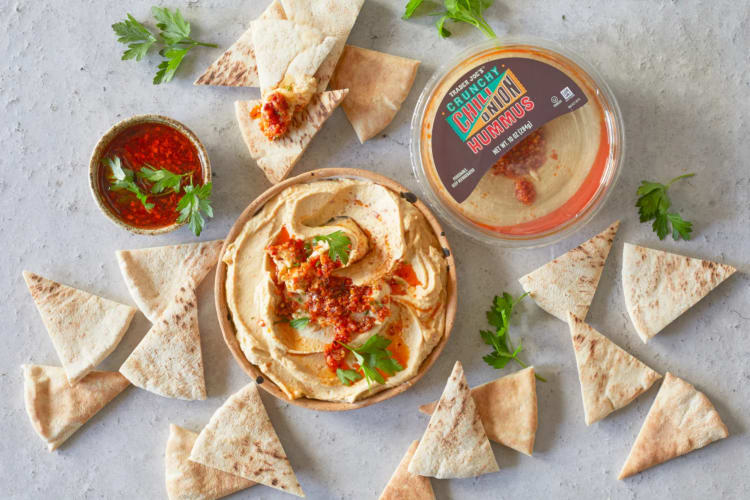 A tub of hummus with chiles and crunchy onions next to pita bread