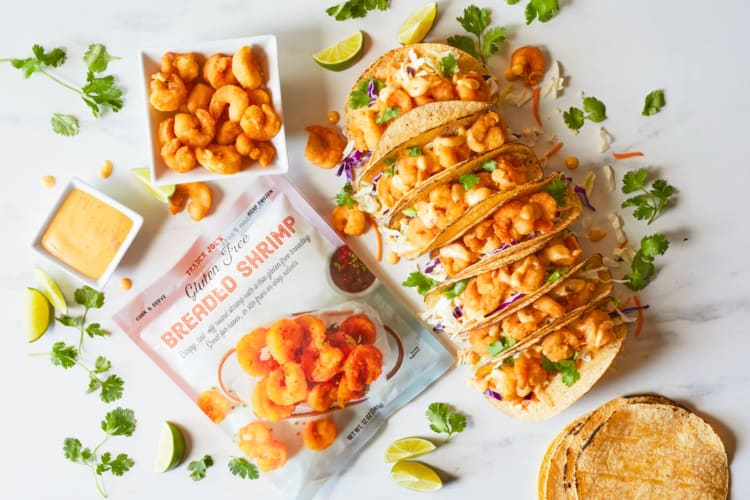 A bag of breaded shrimp next to shrimp tacos 