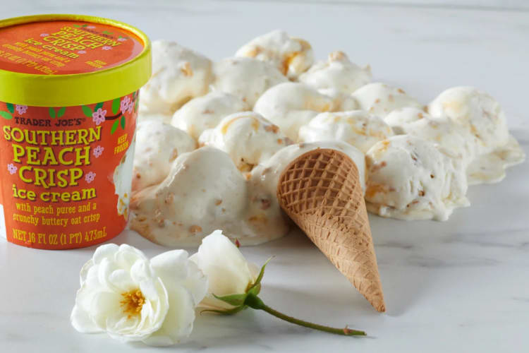 A tub of Southern Peach Crisp ice cream next to ice cream and white flowers