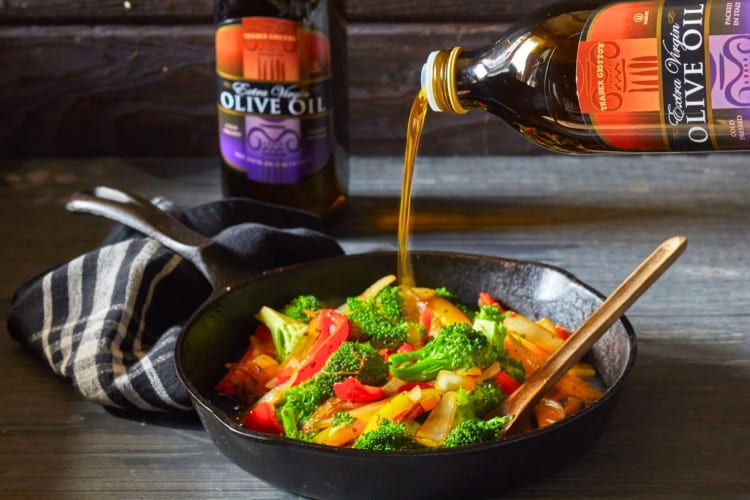 Olive oil being poured onto vegetables in a skillet