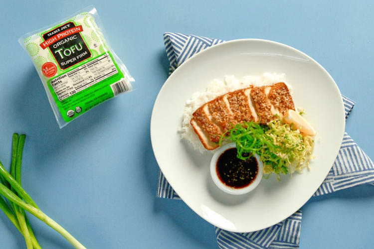 A package of tofu next to a tofu dish and fresh green onions