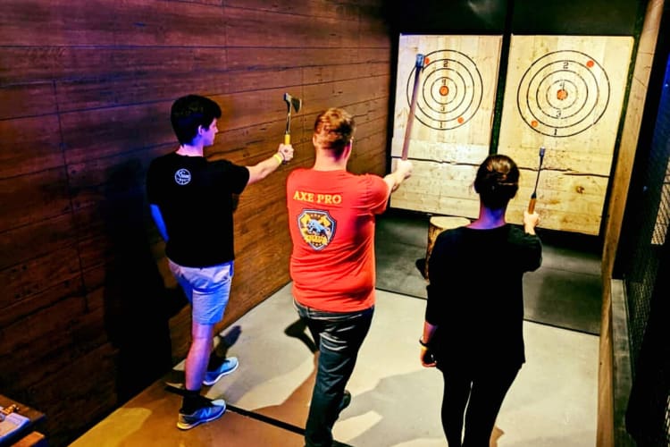 An instructor teaching two people how to throw an axe