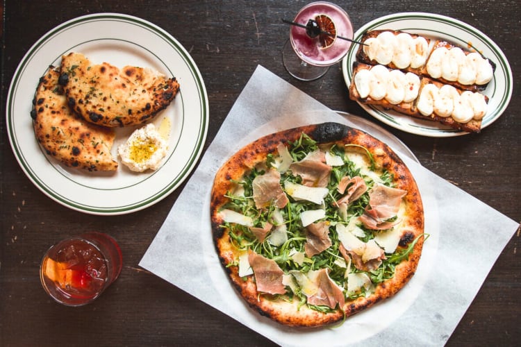 A pizza and other dishes on a table with cocktails