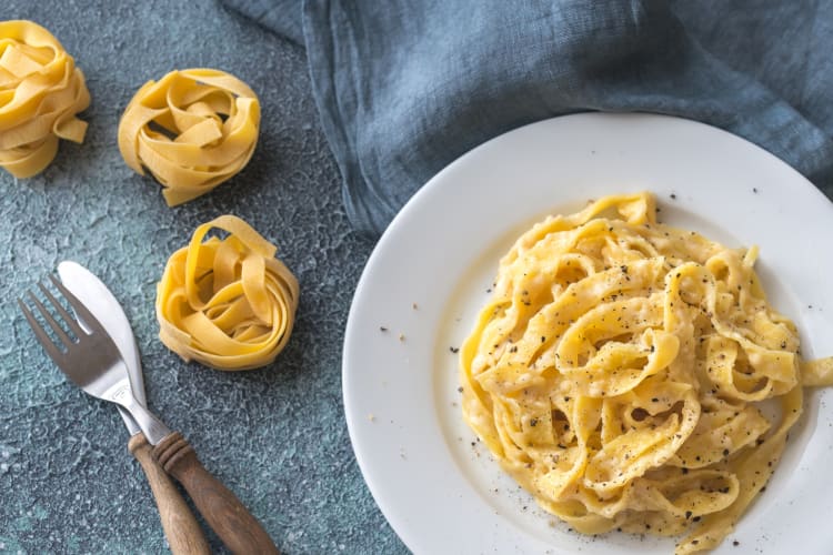 A bowl of fettuccine pasta next to dry fettuccine and cutlery