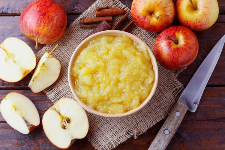 Apple sauce in a bowl surrounded by apples and apple pieces