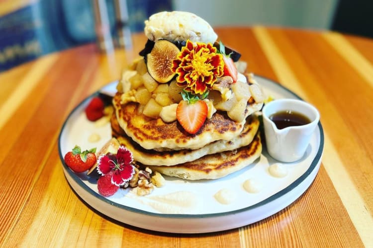 A stack of pancakes with edible flowers and fruit