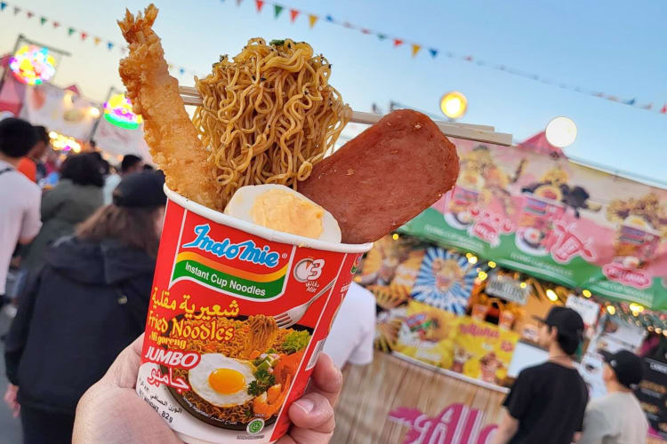 A person holding an instant noodle cup with toppings like tempura shrimp