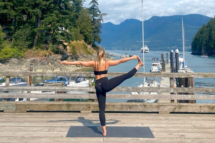 A person stretching on a pier next to water and evergreen trees