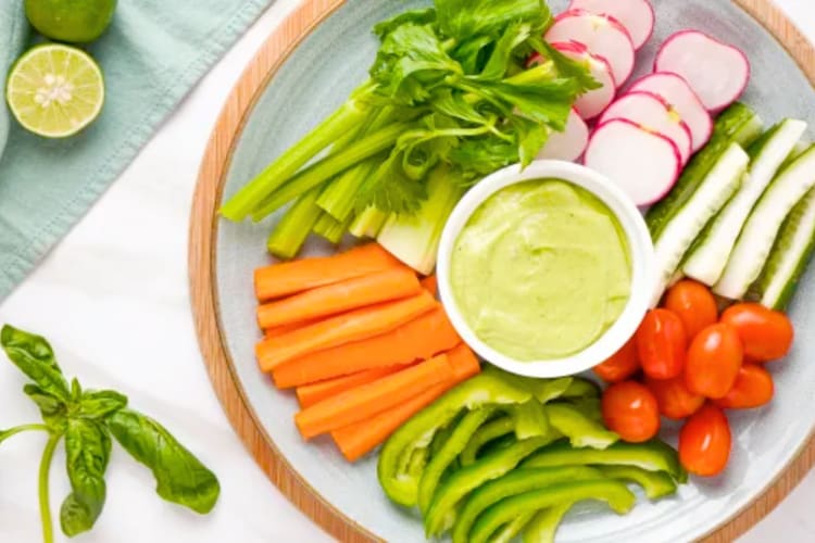 A green dip surrounded by fresh, raw vegetables